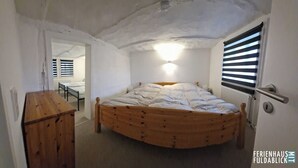 A bedroom with a wooden bed, a nightstand, a radiator, and a window with blinds. - Ferienhaus Fuldablick Das Ferienhaus Inmitten der Altstadt von Rotenburg /fulda (Rotenburg an der Fulda)