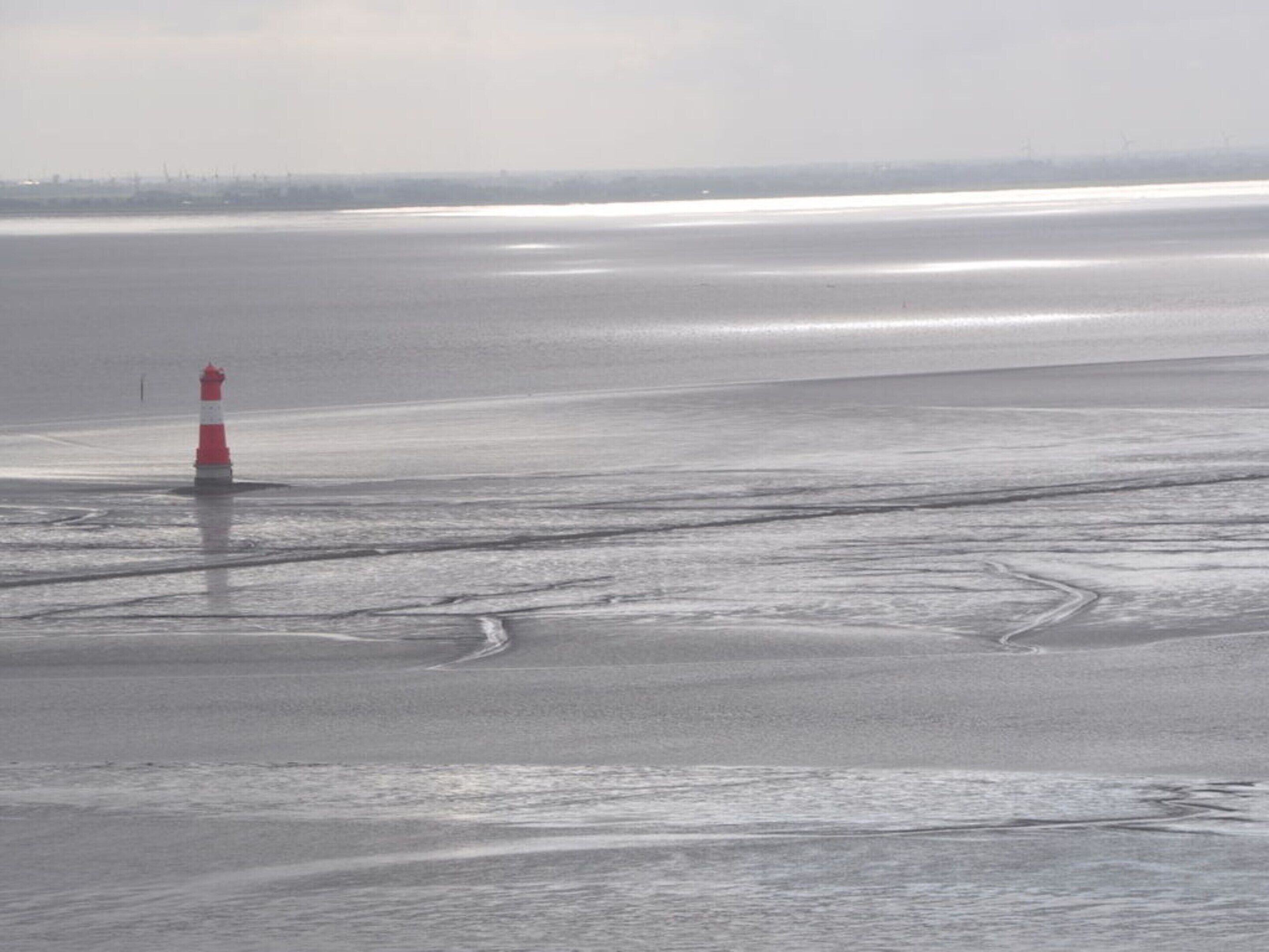 A lighthouse on a frozen body of water with a distant shoreline.