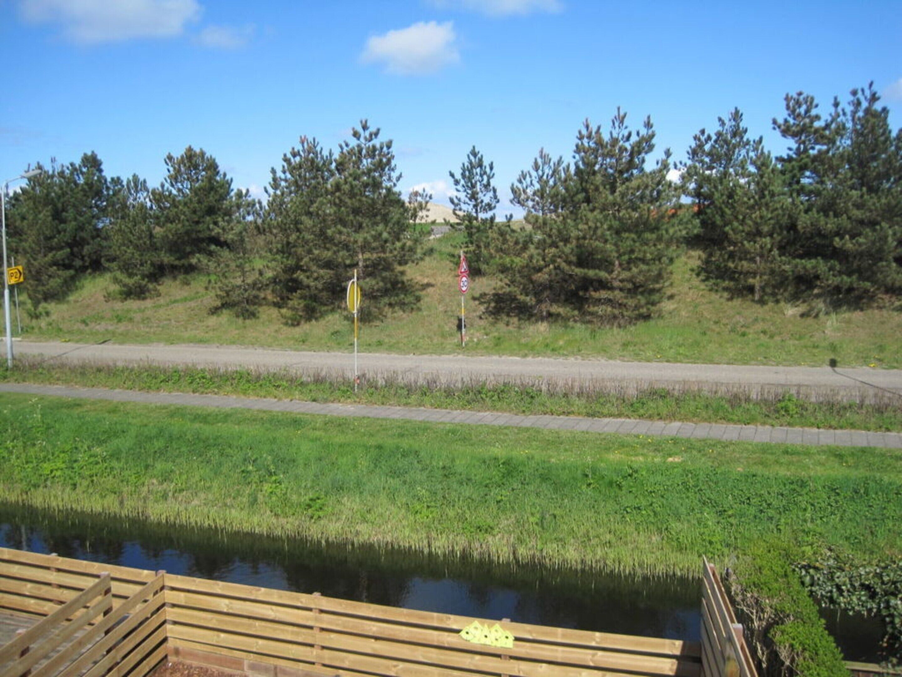 Blick auf einen Fluss mit einer Holzsteganlage, einer Straße und einem Fußweg.