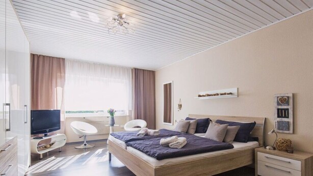 A modern hotel room with a wooden bed, a TV, a desk, and a chair.