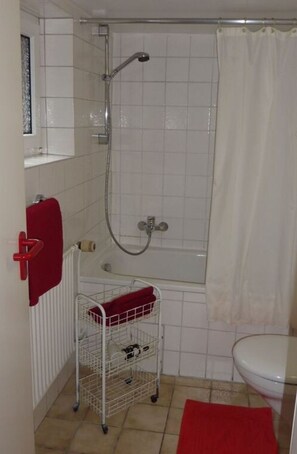 A bathroom with a shower, toilet, and a small sink with a red towel. - Maiken Feikes, \"am Friedrichshain\" 2 (Sylt)