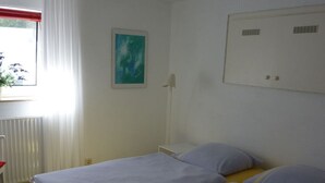 Une chambre avec deux lits, une fenêtre avec des rideaux, un radiateur et un tableau au mur.