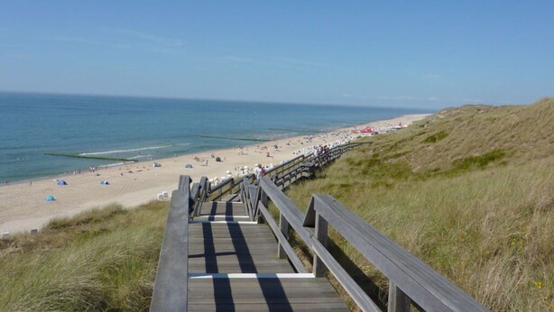 Une promenade en bois menant à une plage où se trouvent des tentes et des parasols.