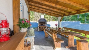 An outdoor patio with wooden benches, a stone fireplace, and a red lantern. - Apartment in Croatia Near the Adriatic Coast (Vinodol)