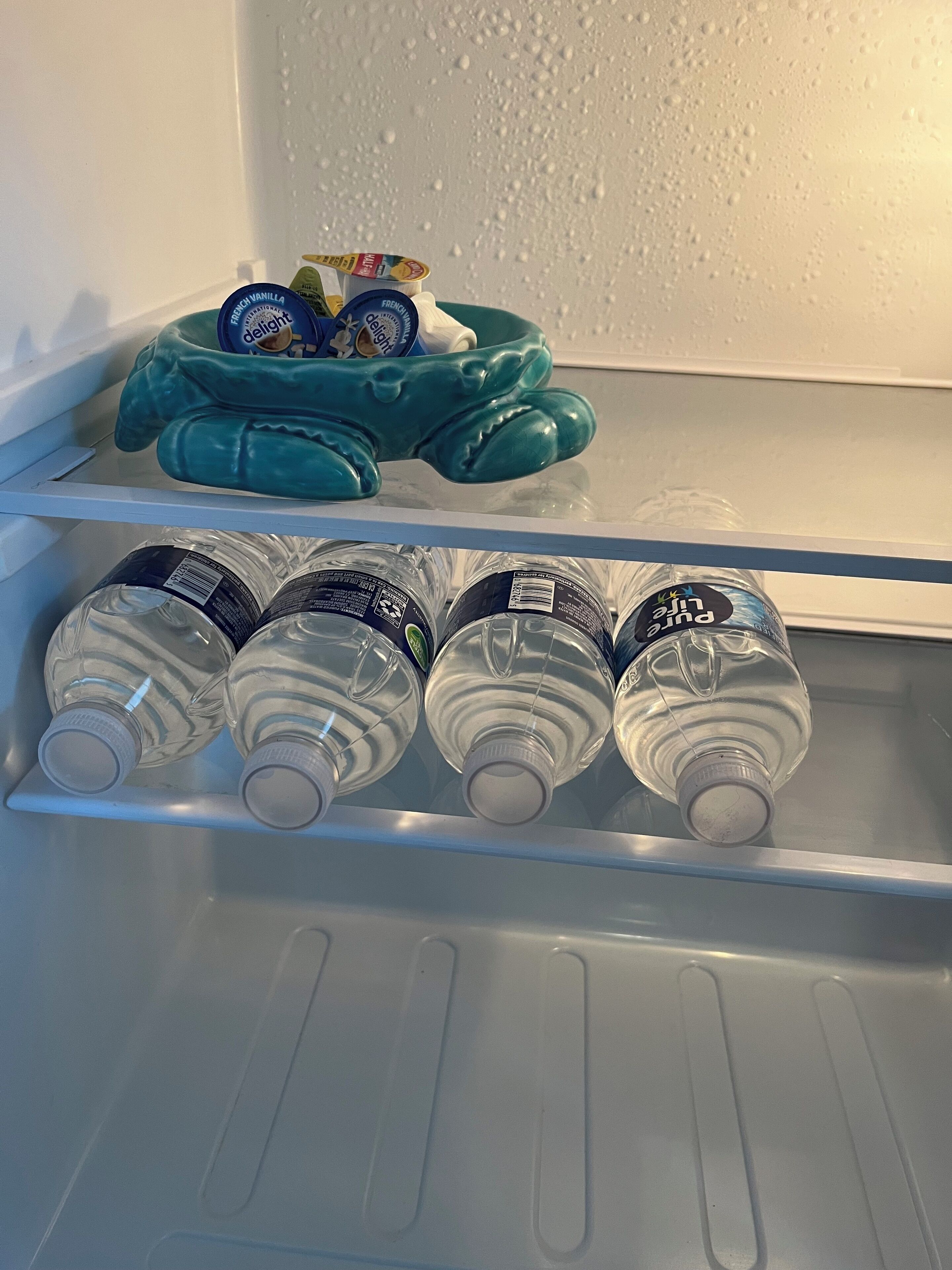 A refrigerator with a teal plush toy and four water bottles on the door shelf.