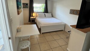 Pieni hotellihuone, jossa on sänky, työpöytä, tuoli, televisio ja kattotuuletin.