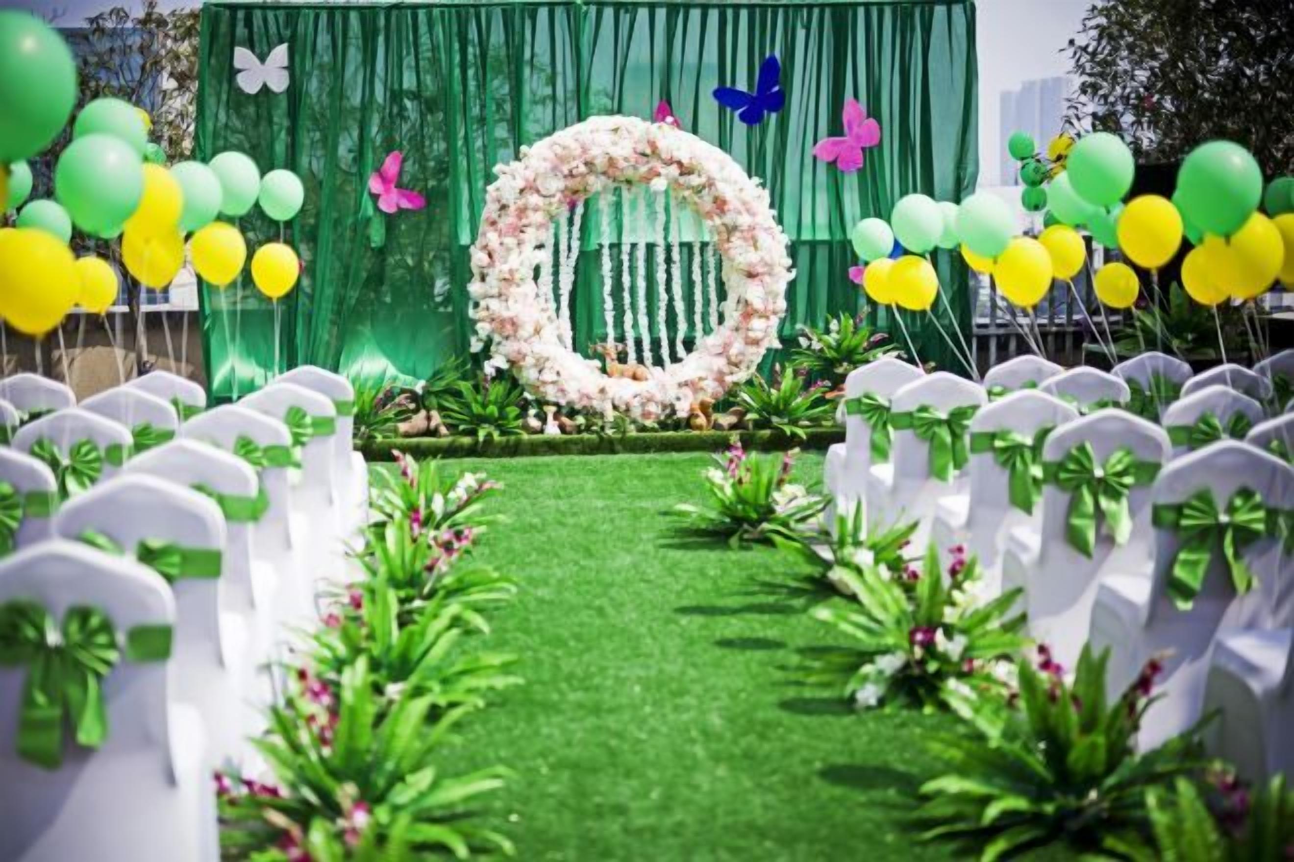 A wedding aisle with white chairs, a green carpet, and a floral arch.