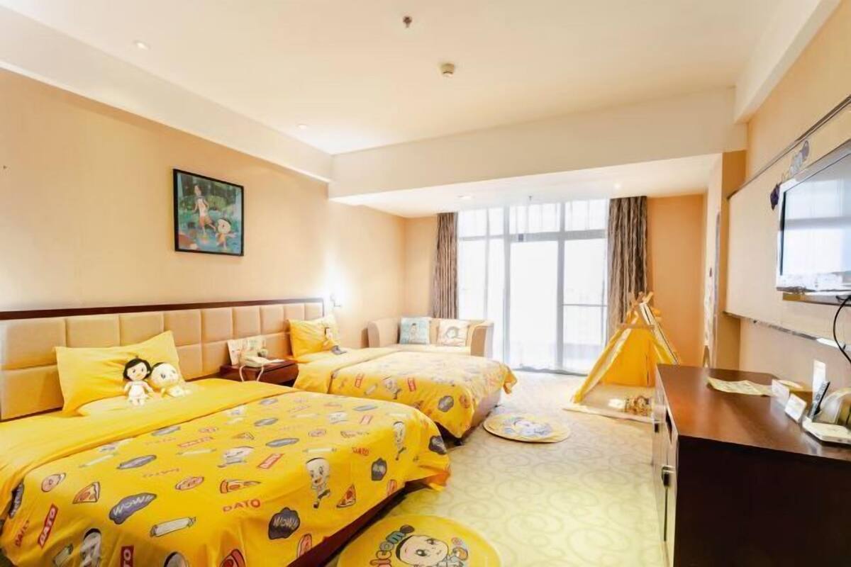 A hotel room with two beds, a desk, a television, and a window with curtains.