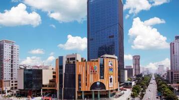 A modern urban area with a prominent skyscraper, a round building with a central atrium, and a busy street with vehicles and pedestrians.