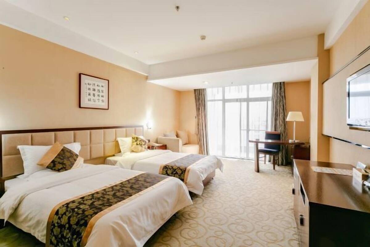 A hotel room with two beds, a desk, a chair, a TV, and a window with curtains.