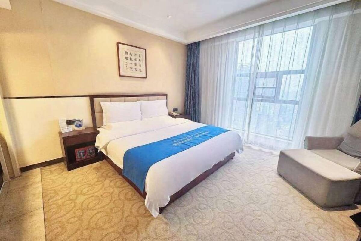 A hotel room with a large bed, a bedside table, a chair, and a window with curtains.