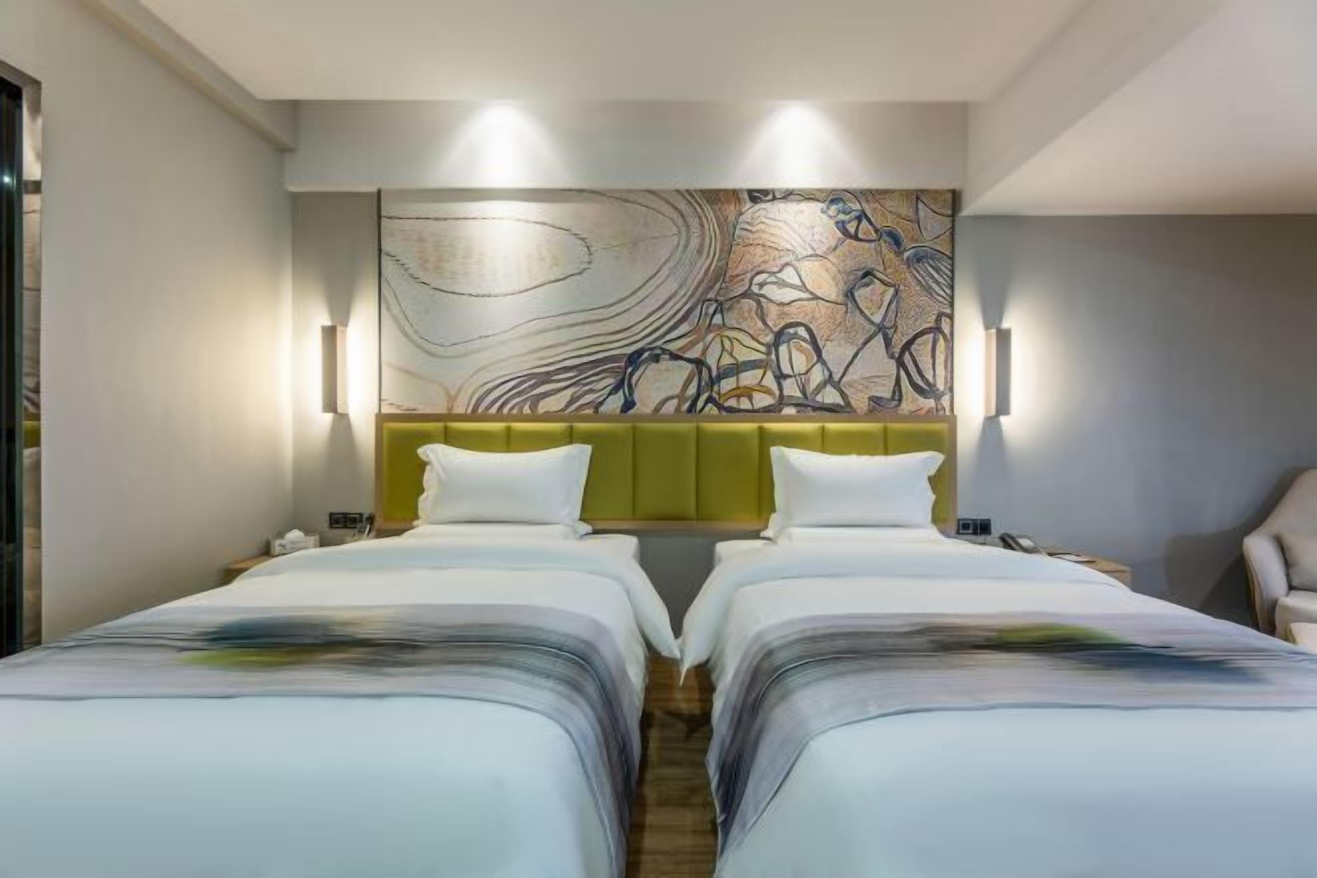 A hotel room with two beds, a large abstract painting on the wall, and a green accent wall.