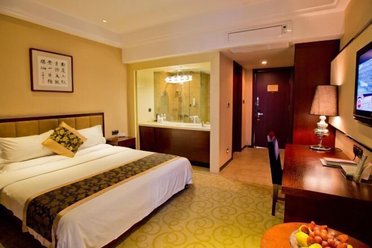 A hotel room with a bed, a desk with a lamp, a television, and a fruit bowl.