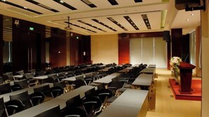A conference room with rows of tables and chairs, a podium, and a stage with a red carpet. - Minsheng Hotel (Yichang)