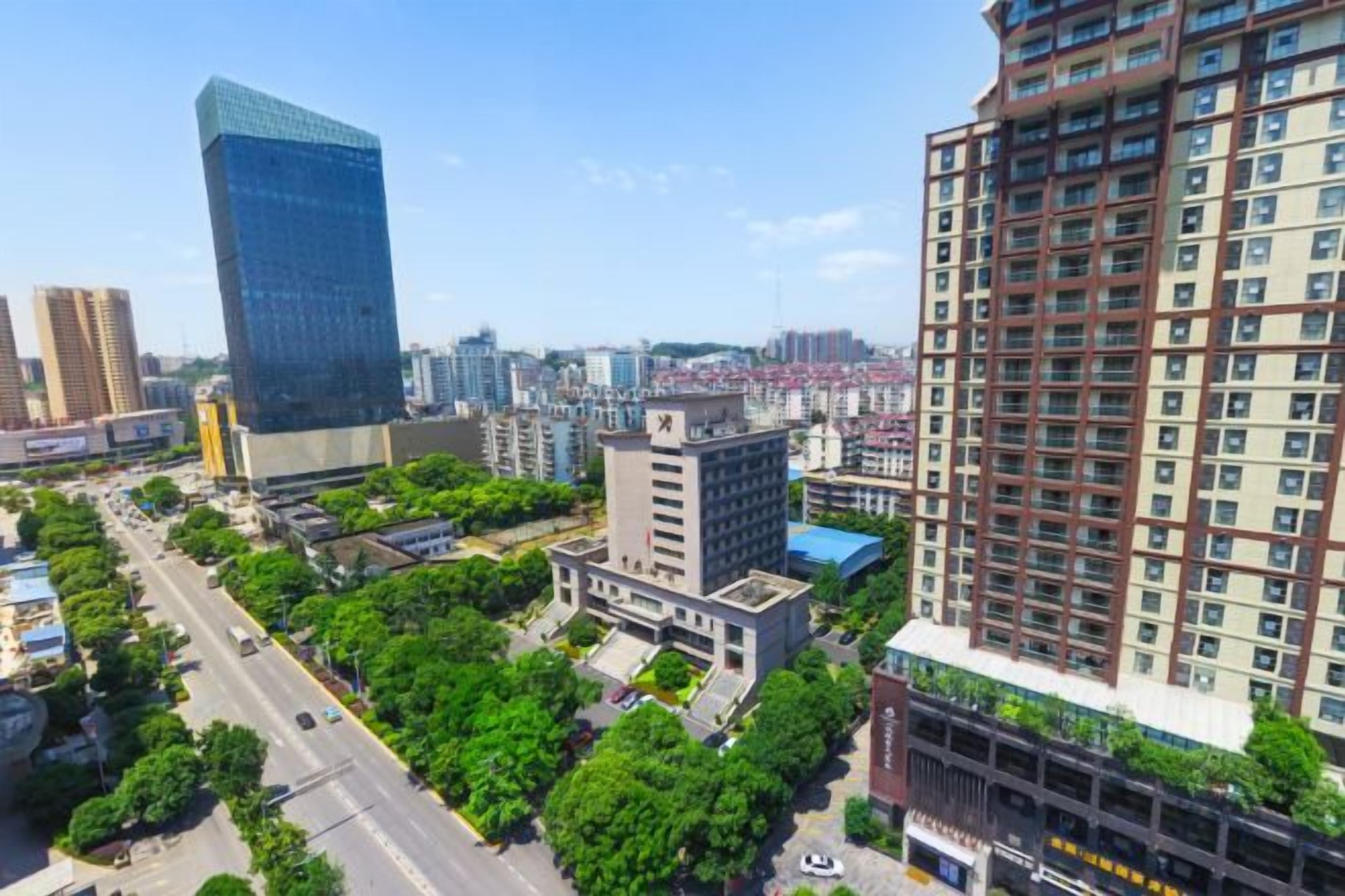 A high-rise building with a modern glass facade, surrounded by smaller buildings and greenery.