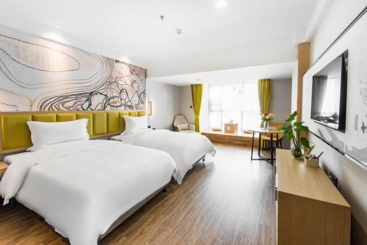 A modern hotel room with two beds, a desk, a chair, and a large window with curtains.