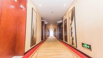A hotel corridor with a red carpet, framed artwork on the walls, and a directional sign.