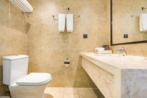 A modern bathroom with beige tiles, a white toilet, a sink with a mirror, and two towels hanging on a towel rack. - Minsheng Hotel (Yichang)