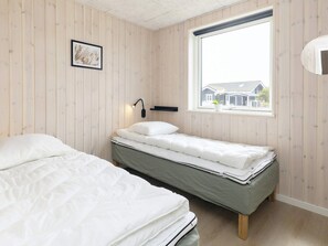 Una habitación con dos camas, una ventana y una lámpara fijada a la pared.
