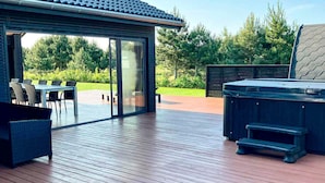 A deck with a hot tub, outdoor furniture, and a glass door leading to a patio area. - 5 Star Holiday Home in Vaeggerlose (Vaeggerlose)