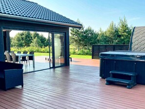 A deck with a hot tub, outdoor furniture, and a glass door leading to a patio area. - 5 Star Holiday Home in Vaeggerlose (Vaeggerlose)