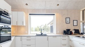 A modern kitchen with white cabinetry, a built-in oven, a large window, and a countertop with a coffee maker and other appliances.
