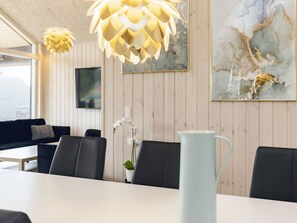 A modern dining area with a white table, black chairs, and a light blue pitcher. - 5 Star Holiday Home in Vaeggerlose (Vaeggerlose)