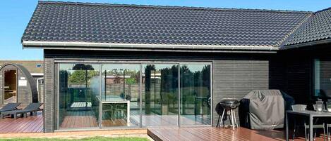 A modern house with a large glass door, a deck, and a barbecue area.