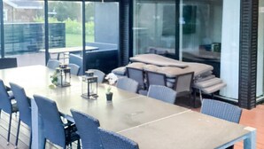 A modern dining area with a large table and chairs, large windows, and a view of greenery outside. - 5 Star Holiday Home in Vaeggerlose (Vaeggerlose)