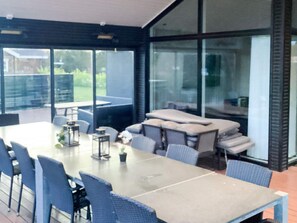 A modern dining area with a large table and chairs, large windows, and a view of greenery outside. - 5 Star Holiday Home in Vaeggerlose (Vaeggerlose)