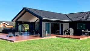 A modern house with a covered patio, a barbecue area, and a well-maintained lawn. - 5 Star Holiday Home in Vaeggerlose (Vaeggerlose)