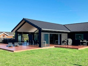 A modern house with a covered patio, a barbecue area, and a well-maintained lawn. - 5 Star Holiday Home in Vaeggerlose (Vaeggerlose)