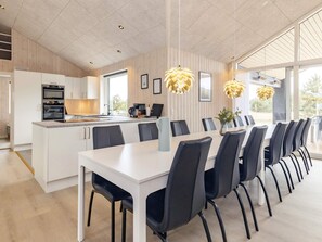 Una cocina moderna con electrodomésticos integrados, un comedor con una mesa larga y sillas, y ventanas grandes que dejan entrar luz natural.