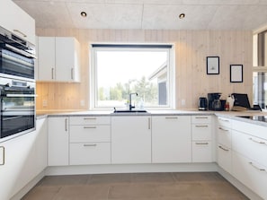 A modern kitchen with white cabinetry, a built-in oven, a large window, and a countertop with various appliances.