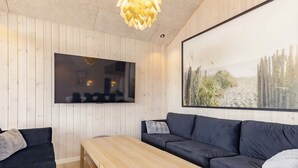 A modern living room with a wooden table, dark sofa, and a large framed picture on the wall. - 5 Star Holiday Home in Vaeggerlose (Vaeggerlose)