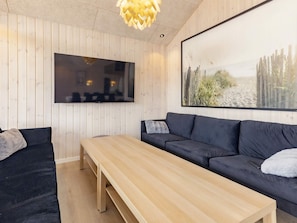 A modern living room with a wooden table, dark sofa, and a large framed picture on the wall. - 5 Star Holiday Home in Vaeggerlose (Vaeggerlose)