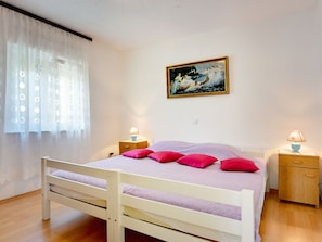 A bedroom with a single bed, two bedside tables, a nightstand, a painting on the wall, and a window with sheer curtains. - Apartment With Balcony and sea View (Medulin)
