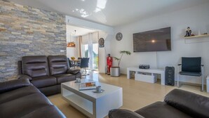 A modern living room with a stone wall, leather sofas, a flat-screen TV, and a dining area visible through an open door. - Gusto Comfortable Holiday Residence (Vodnjan)