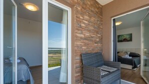 A balcony with a wicker chair, a bed with a gray bedspread, and a view of the landscape. - Gusto Comfortable Holiday Residence (Vodnjan)