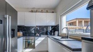 A modern kitchen with white cabinets, a black marble backsplash, and a stainless steel refrigerator. - Gusto Comfortable Holiday Residence (Vodnjan)