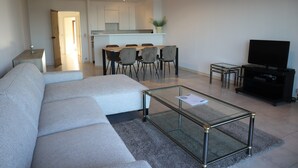 A modern living room with a sofa, a glass coffee table, a TV, and a dining area with chairs and a table. - Apartment in Nieuwpoort With Sea Views (Nieuwpoort)