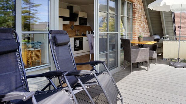 A modern outdoor patio with a dining table and chairs, a sliding glass door leading to a kitchen, and a white umbrella providing shade. - Holiday Home by the Baltic Sea (Zingst)