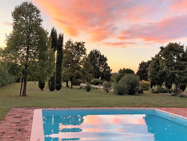 A swimming pool with a brick border, surrounded by a grassy area and trees. - Belvilla by OYO Ca' Landrini (Vo)