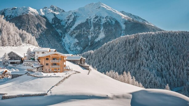 A snow-covered mountain landscape with a wooden lodge featuring multiple balconies and a ski slope in the foreground. - Biologische Pension & Boerderij "de Veitenhof" (Umhausen)