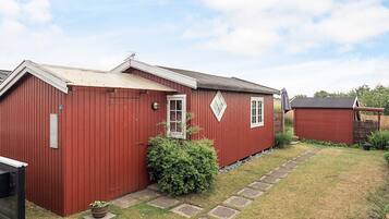 A red building with a small window and a door, a paved pathway, and a bush in the yard.