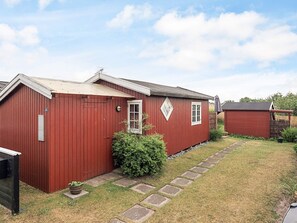 A red building with a small window and a door, a paved pathway, and a bush in the yard.