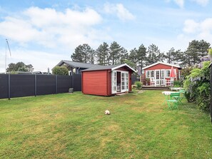 A red wooden shed, a green lawn, and a white fence in a backyard.