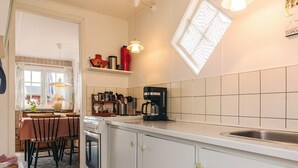 A compact kitchen with white cabinets, a coffee maker, and a window with a decorative screen. - 3 Person Holiday Home in Karrebaeksminde (Karrebæksminde)