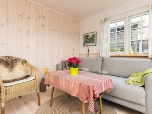 A cozy room with a checkered table, a wicker chair, a grey sofa, and a window with curtains.
