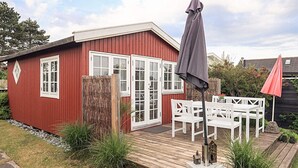 A red wooden building with white-framed windows, a deck with outdoor furniture, and a small garden area. - 3 Person Holiday Home in Karrebaeksminde (Karrebæksminde)